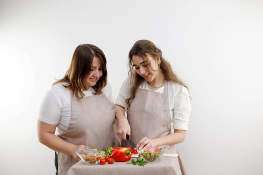 women mother and daughter preparing salad Mom daughter cuts red bell pepper identical kitchen aprons space for text teaching cooking school household delicious food fruit and vegetable store grocery photo