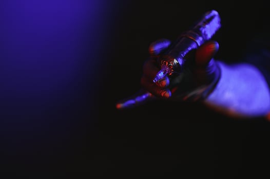 Closeup of tattooer master's hand in black glove holding machine for making tattoo art on body isolated on dark background in neon. photo