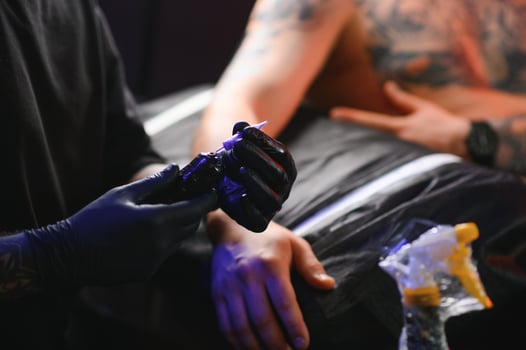 Male tattoo artist holding a tattoo gun, showing a process of making tattoos on a male tattooed model's arm photo