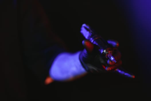 Closeup of tattooer master's hand in black glove holding machine for making tattoo art on body isolated on dark background in neon. photo