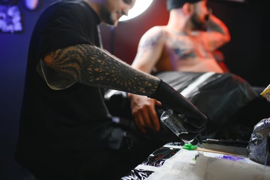bearded tattoo artist working at his studio tattooing sleeve on the arm of his male client. Man getting tattooed by professional tattooist photo