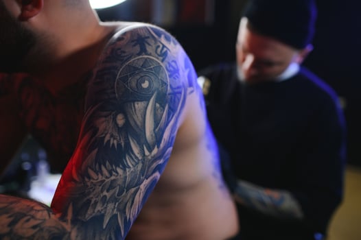 Shot of a tattoo artist and a mans back totally tattooed with black ink photo