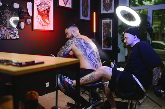 Shot of a tattoo artist and a mans back totally tattooed with black ink photo