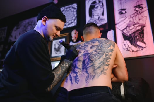 Tattoo artist man with black gloves draws a knight tattoo on the guy's back in the studio. Tattoo artist's workflow photo