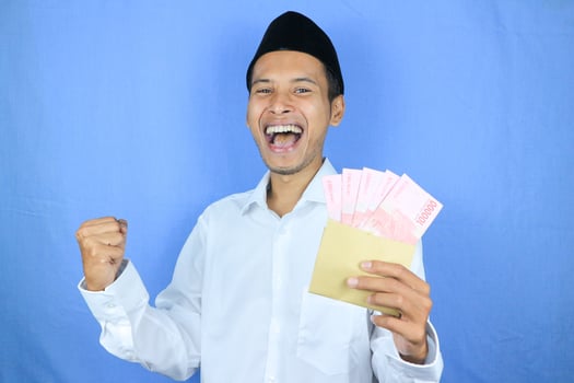 Happy expression of Asian Muslim man holding money rupiah banknotes isolated on white background photo
