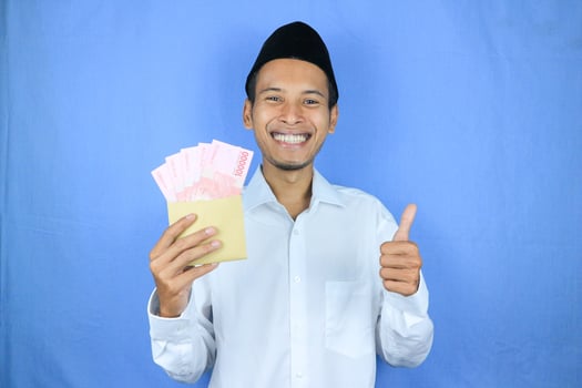 Happy expression of Asian Muslim man holding money rupiah banknotes isolated on white background photo