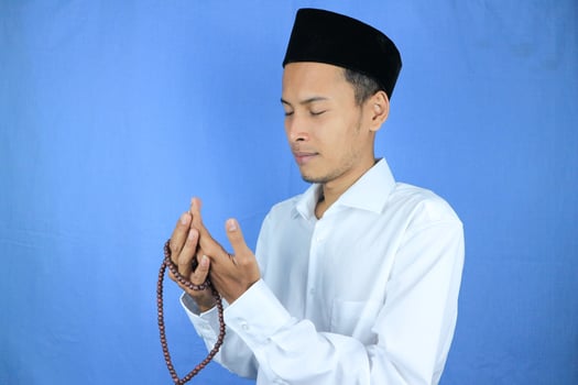 Muslim asian man holding prayer beads on blue background. Ramadan kareem and ied mubarak concept. photo