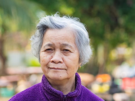 Portrait of elderly Asian woman with short gray hair and standing smiling and looking at the camera while standing in a garden. Space for text. Concept of aged people and relaxation photo