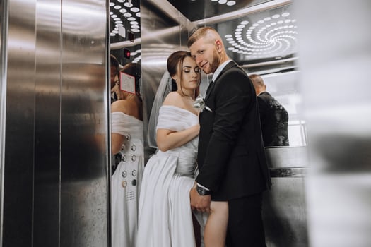 A bride and groom are in an elevator, the bride is wearing a white dress photo