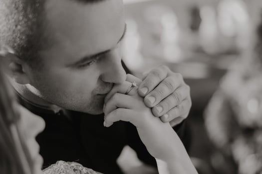 A man kisses a woman's hand, and she is wearing a ring photo