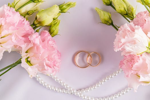 Two gold classic wedding rings on a white satin background with fresh pink austoma flowers. A copy space. postcard. invitation. cover. photo