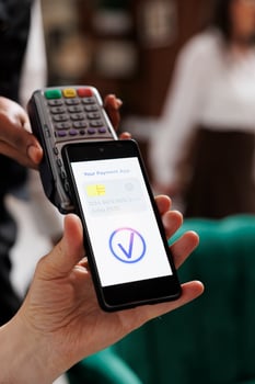 Detailed view of concierge helping elderly retired man with payment using cellphone and NFC technology. Close-up shot of male traveler paying using mobile device with assistance of hotel employee. photo