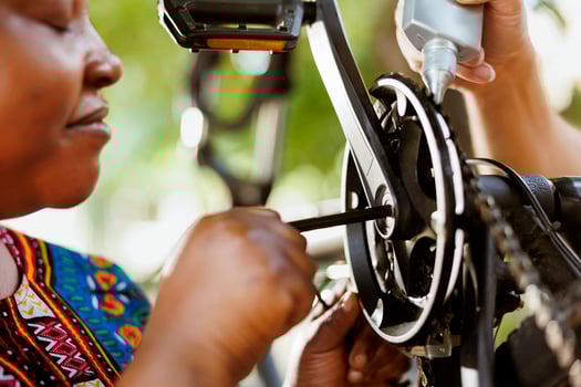 Close up of female african american using allen key to repair damaged bicycle crank-arm. Outdoor detailed shot of two people repairing and greasing bike chain and pedals for secure outdoor cycling. photo