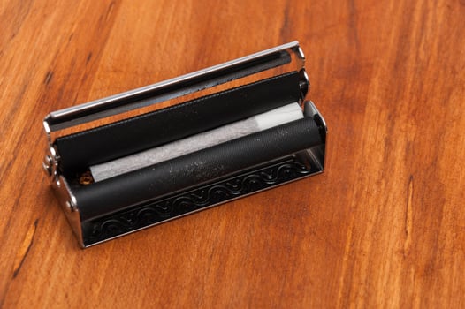 Hand rolled cigarette in the machine on the wooden background photo