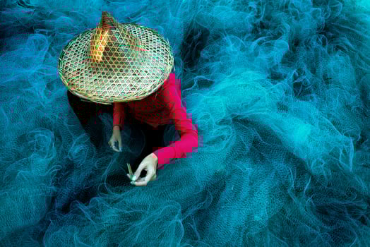 Women fisherman hands sewing blue fishing nets sitting on the ground and surrounded big net photo