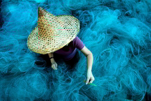 Women fisherman hands sewing blue fishing nets sitting on the ground and surrounded big net photo