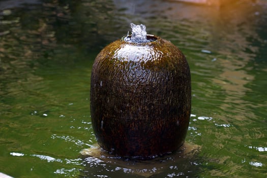 Ceramic fountain jar installed at the pond in the garden of the house. It is pottery for decorating houses and gardens to be beautiful, shady, natural and enhance feng shui. photo
