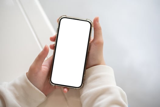 A woman in a white sweater holding a smartphone white-screen mockup over a white table indoors. photo