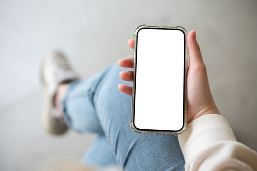 A close-up image of a woman in jeans sits indoor and uses her smartphone. photo