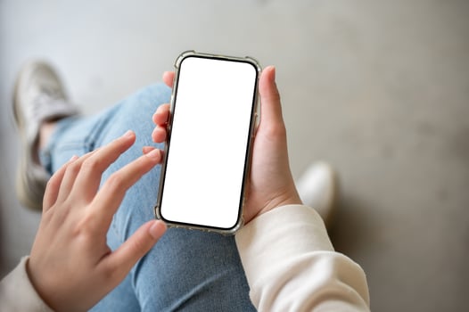 A close-up image of a woman in jeans sits indoor and uses her smartphone. photo