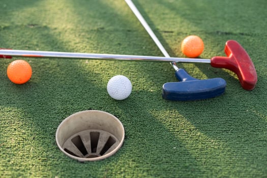 Assorted miniature golf putters and balls askew on synthetic grass. photo