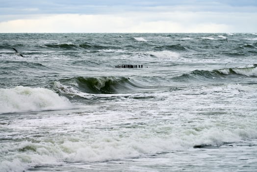 View of blue sea with foaming waves and wooden breakwaters photo