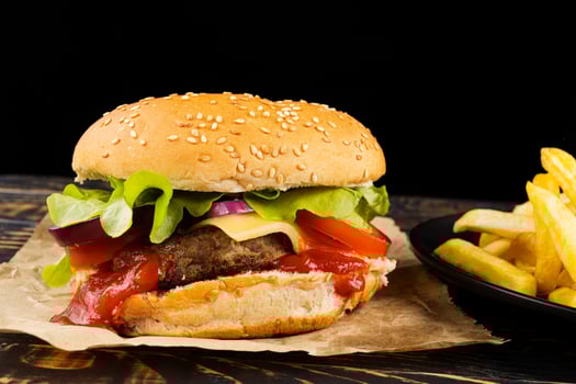 Burger with cutlet, tomato, cheese and greens. Fresh tasty burger isolated on black background photo
