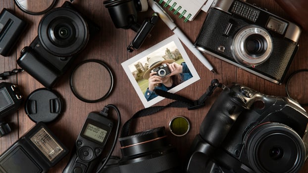 Photograph of young woman taking a photo, surrounded by flash, filters, lenses, modern and old cameras on a wooden table photo
