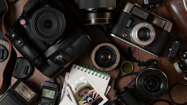 Photograph of young woman taking a photo, surrounded by flash, filters, lenses, modern and old cameras on a wooden table photo