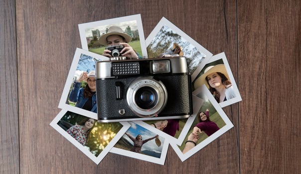 Old photo camera surrounded by photographs of women in different places on a dark wooden table