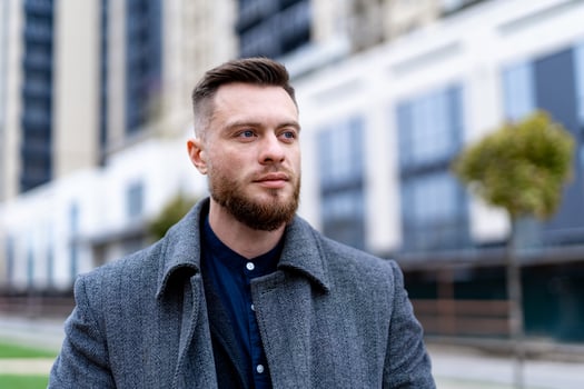 Outdoor fashion male portrait. Handsome and charming young businessman dressed in suit and coat standing outside a modern building. Head and shoulders portrait. photo