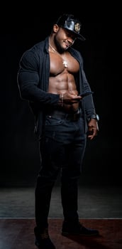 Strong athlete in dark jeans poses to the camera on black background. Unbuttoned black shirt and perfect abs. Portrait of an afro american bodybuilder with phone in hands. photo