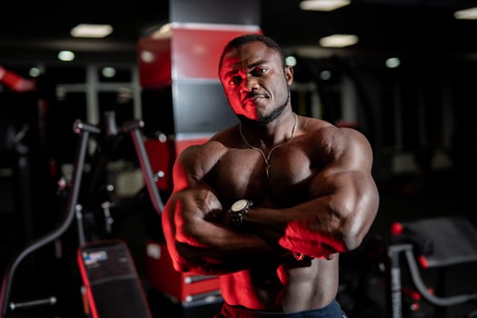 Athlete with strong body poses cross hands on modern gym background. Front view on very muscular pumped up fitness model. photo