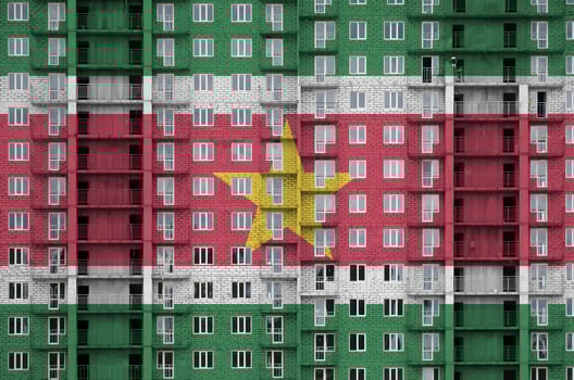 Suriname flag depicted in paint colors on multi-storey residental building under construction. Textured banner on brick wall background photo
