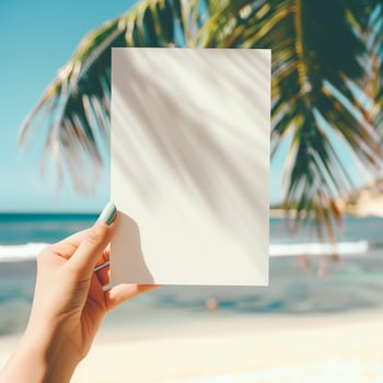 Blank paper in hand with palm trees and beach in background. photo
