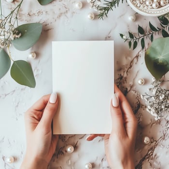 A photo of hands holding a blank notecard with a marble background and floral decorations.