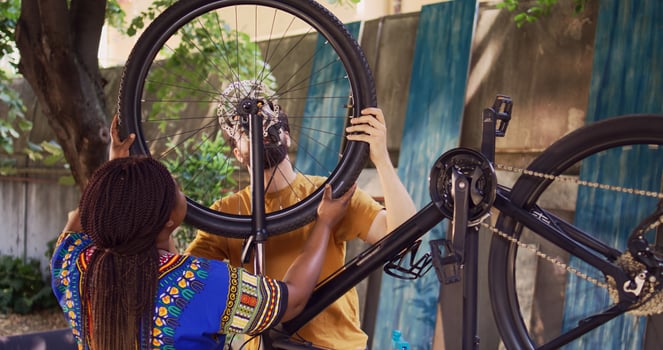 Dedicated boyfriend and girlfriend doing annual maintenance on bike tires for safe cycling in home yard. Youthful multiracial pair successfully mounting wheel on modern bicycle frame. photo