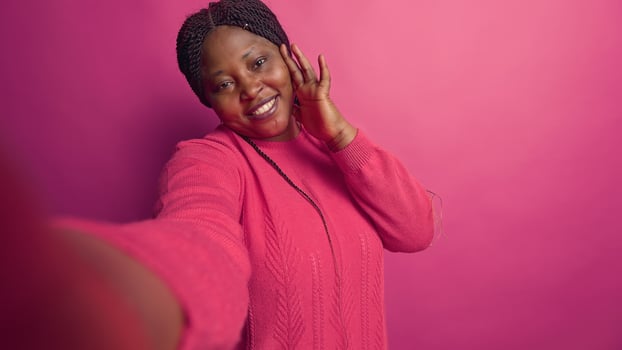 POV of african american fashion blogger grasping mobile phone on call doing random cute hand gestures. Beautiful black woman in pink sweater using smartphone for selfies. photo
