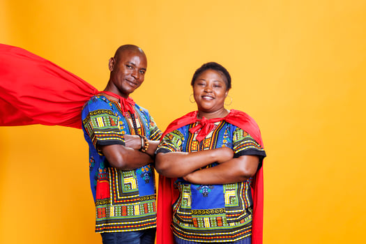 Smiling black couple dressed in superhero red cloaks posing with folded hands and looking at camera. Cheerful superman and superwoman pair wearing capes showing power and strength portrait photo