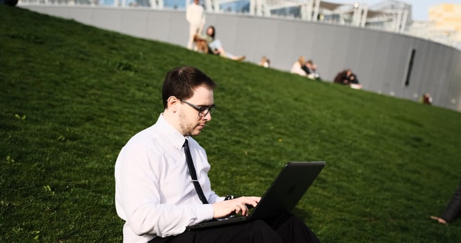 Caucasian bearded business man freelancer working on break with laptop outdoors in park. Male office worker sitting on a green grass on a city park on a modern urban background Workplace outside photo