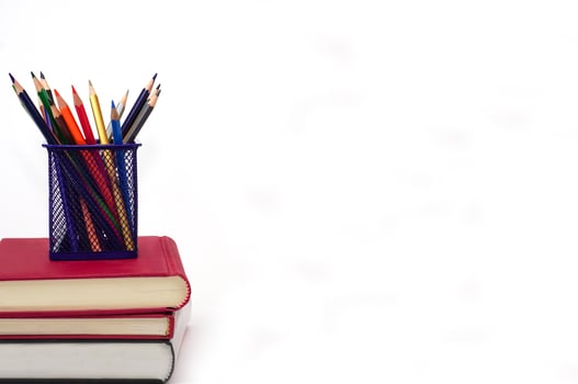 Crayon or colored pencils in box laying on a stack of books, white background. Knowledge and education concept. photo