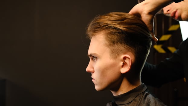 Barber shop. Man in barber's chair, hairdresser prepare his hair with comb for cutting and styling it. Concept Barbershop. side view in dark key lightning with warm light photo