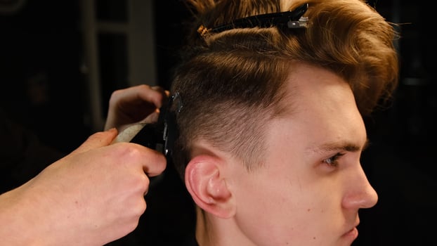 men's hairstyling and haircutting with hair clipper in a barber shop or hair salon. Hairdresser service in a modern barbershop in a dark key lightning with warm light side view photo
