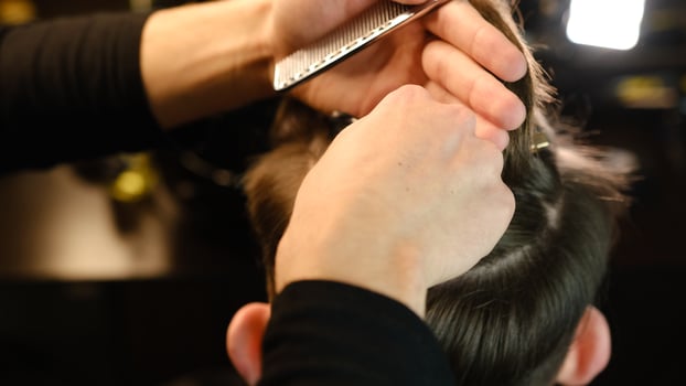 Closeup View Of barber using hair clip to fix the hair for cut and styling it. Hairdresser use pinsn hair salon. service in a modern barbershop in a dark key lightning with warm light back view photo