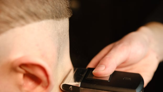 close up men's hairstyling and haircutting with barber shaving machine, hair cut for male. Hairdresser service with shaver in a modern barbershop in a dark key lightning with warm light side view photo