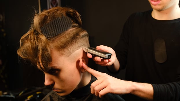 men's hairstyling and haircutting with barber shaving machine, hair cut for male. Hairdresser service with shaver in a modern barbershop in a dark key lightning with warm light side view photo