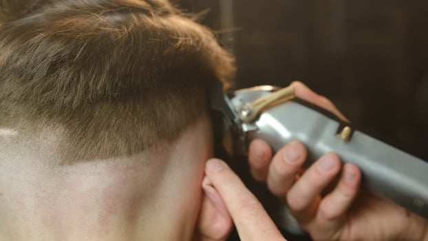 close up men's hairstyling and haircutting with hair clipper in a barber shop or hair salon. Hairdresser service in a modern barbershop in a dark key lightning with warm light and smoke back view photo