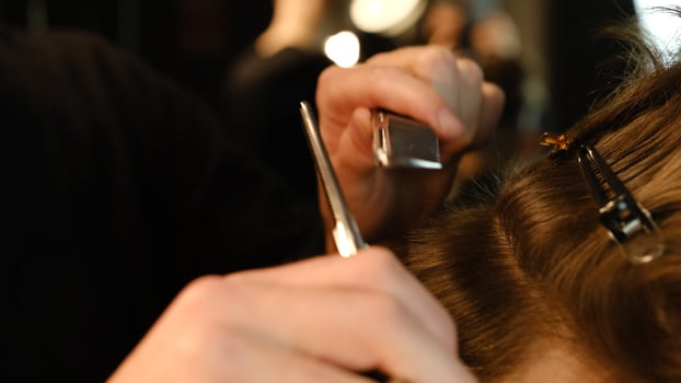 Close up Barber use Thinning scissors and metal comb on brown wavy hair of young man. Hairdresser service in a modern barbershop in a dark key lightning with warm light side view photo
