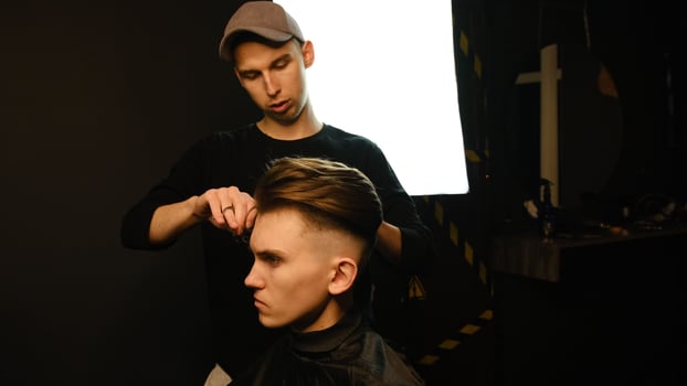 Barber master hairdresser does hairstyle and style with scissors and comb. Concept Barbershop. side view in dark key lightning with warm light photo