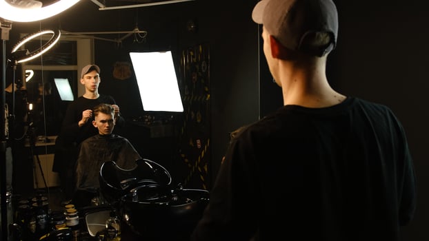 Young barber talking to teenage client in armchair in barbershop decide on what hair style he want. Hairdresser talking with customer about hair style back view photo